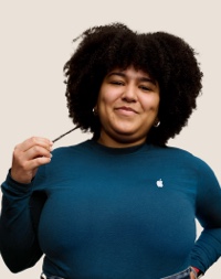 Portrait of a smiling Apple Retail team member with long, curly dark hair.