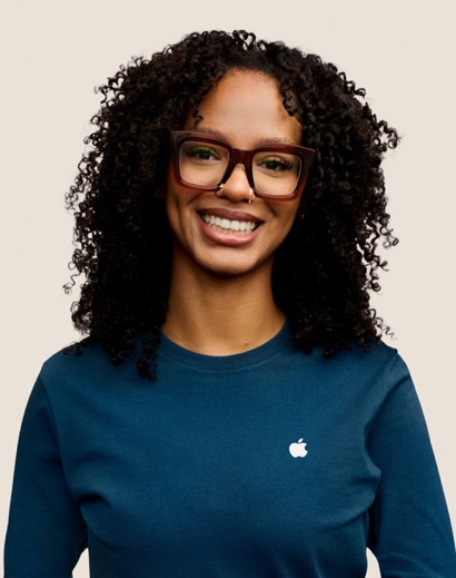 Portrait of a smiling Apple Retail team member with long, curly dark hair and eyeglasses.