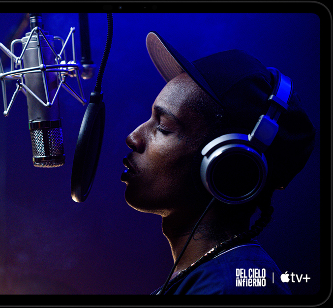 Un iPad Pro, posición horizontal, parte frontal, color negro espacial, esquinas redondeadas, marco de la pantalla negro, la pantalla muestra la app  AppleTV reproduciendo una escena de una película de Apple TV Highest 2 Lowest con ASAP Rocky como Yung Felon rapeando frente a un micrófono