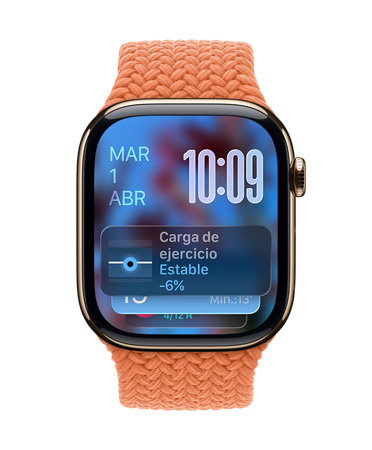 Apple Watch de titanio color oro con una correa trenzada color mandarina, cuya carátula muestra la fecha en la esquina superior izquierda, la hora con números angostos en la esquina superior derecha y debajo el widget Carga de Entrenamiento, todo con el diseño translúcido de Liquid Glass