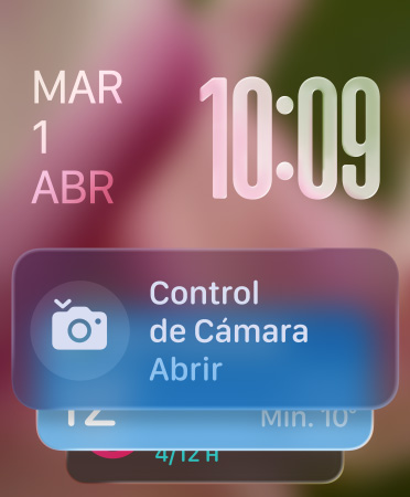 El widget de Control de Cámara aparece en la parte inferior de la pantalla, los números translúcidos de la hora en la parte superior derecha y la fecha en la parte superior izquierda
