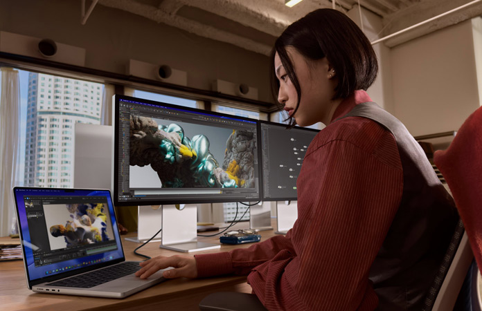 En person som arbetar i en kontorsmiljö med en MacBook Pro som är ansluten till Studio Display XDR