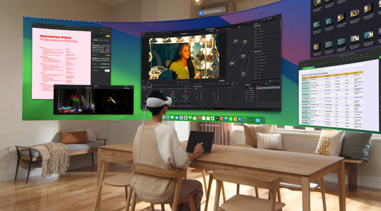 Apple Vision Proを装着した人が13インチMacBook Proを開いてデスクに座っている。画面の内容が表示されたカーブしたウルトラワイドディスプレイが部屋に投影されている