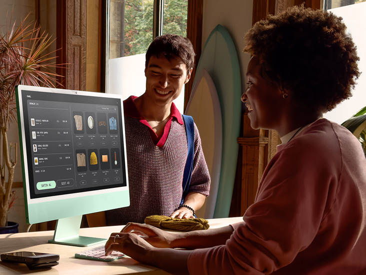 İyi aydınlatılmış bir odada bulunan iki kişiden biri, yeşil iMac M4 ekranında bir siparişi kontrol ediyor.