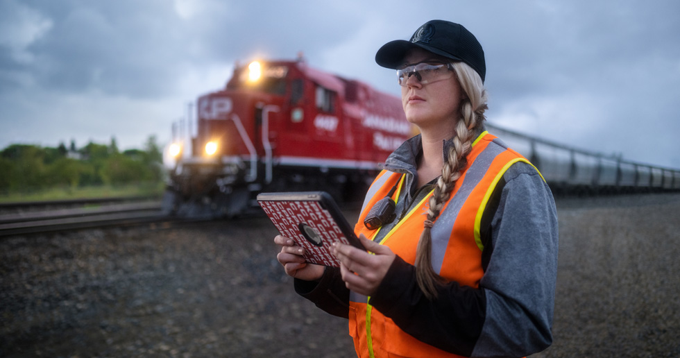 Une employée des chemins de fer regarde les voies en tenant un iPad pendant qu’un train passe