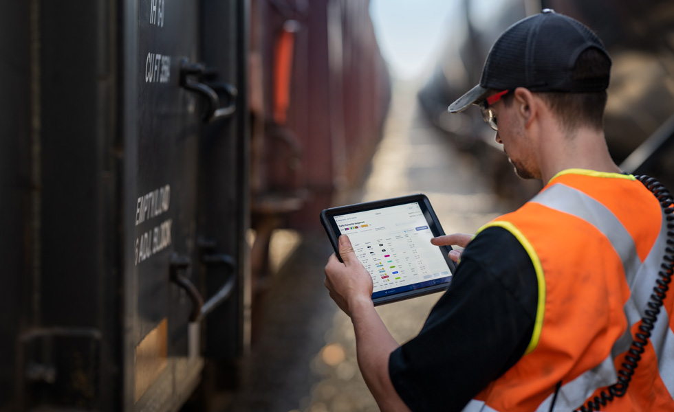 Un cheminot à côté d’un train consulte un iPad qui affiche une grille d’horaires