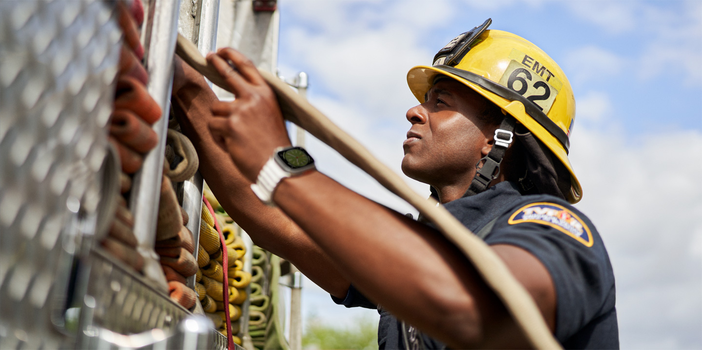 A firefighter pulls a hose out of a fire truck while wearing an Apple Watch