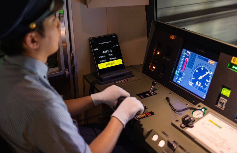 Một chiếc iPad hiển thị các ga tàu và giờ tàu chạy gần bảng điều khiển, có người lái tàu đang làm việc ở đó.