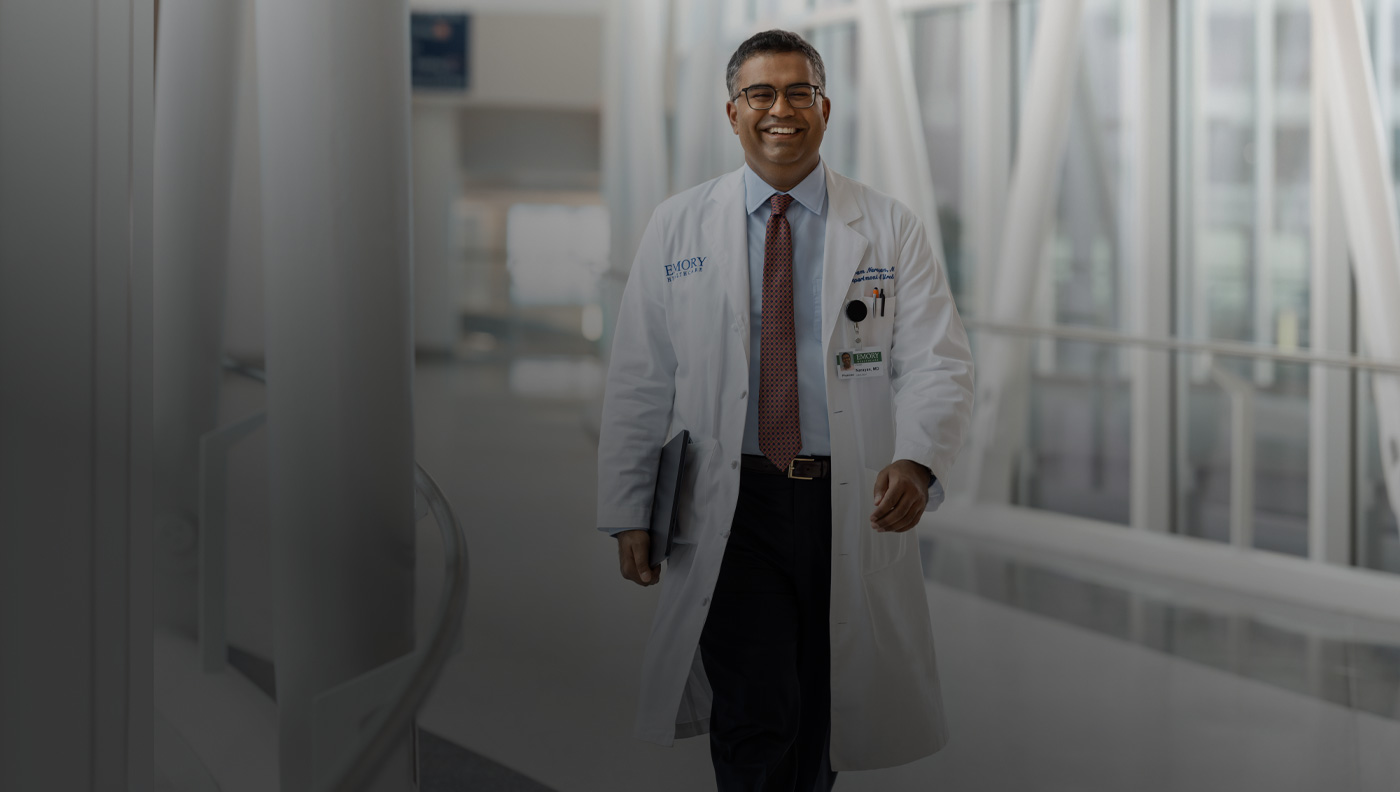 A doctor holding a MacBook under their right arm while walking.