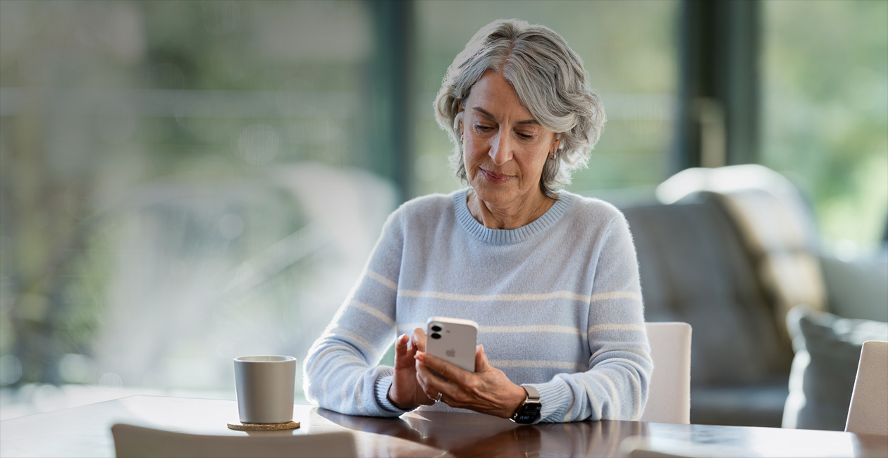 Une femme, accoudée à une table, regarde son iPhone.