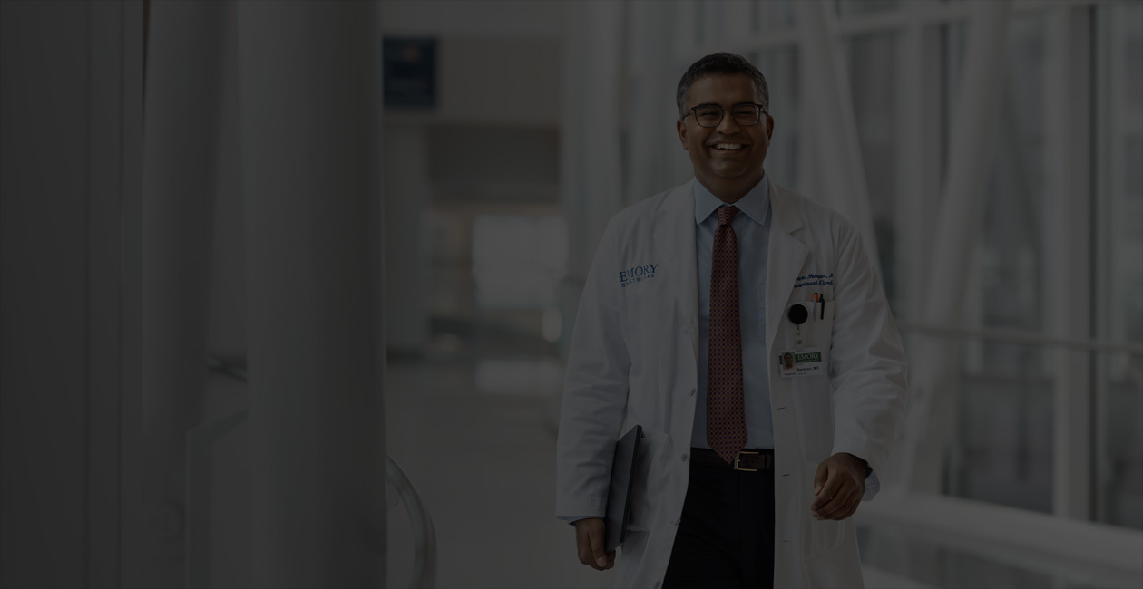 Un médecin marche en tenant un MacBook sous son bras droit.