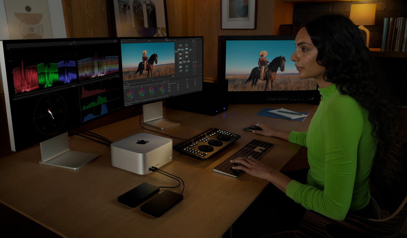 Ein Profi ist mit einem Mac Studio verbunden, bearbeitet Dateien und nutzt dabei drei Displays