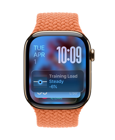 Apple Watch rosa-dourado com bracelete entrançada tangerina. O mostrador apresenta a data no canto superior esquerdo, a hora com números empilhados no canto superior direito, widget Carga de treino na parte inferior, tudo em Liquid Glass transparente